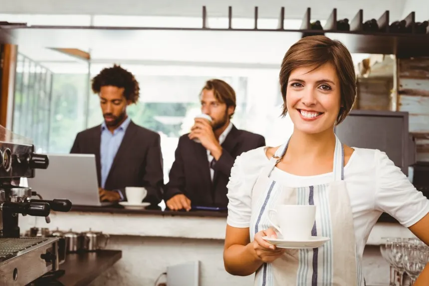 Female barista holding coffee cup with patrons in background Business directory